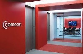 Red-themed Comcast office entrance featuring a logo on the wall and a conference room visible through glass doors