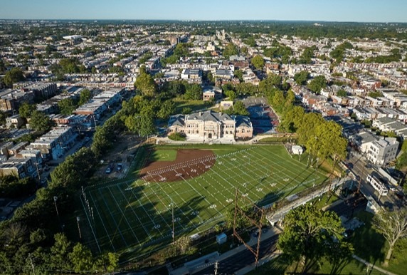 Aerial view of a sports field adjacent to a historic brick school building