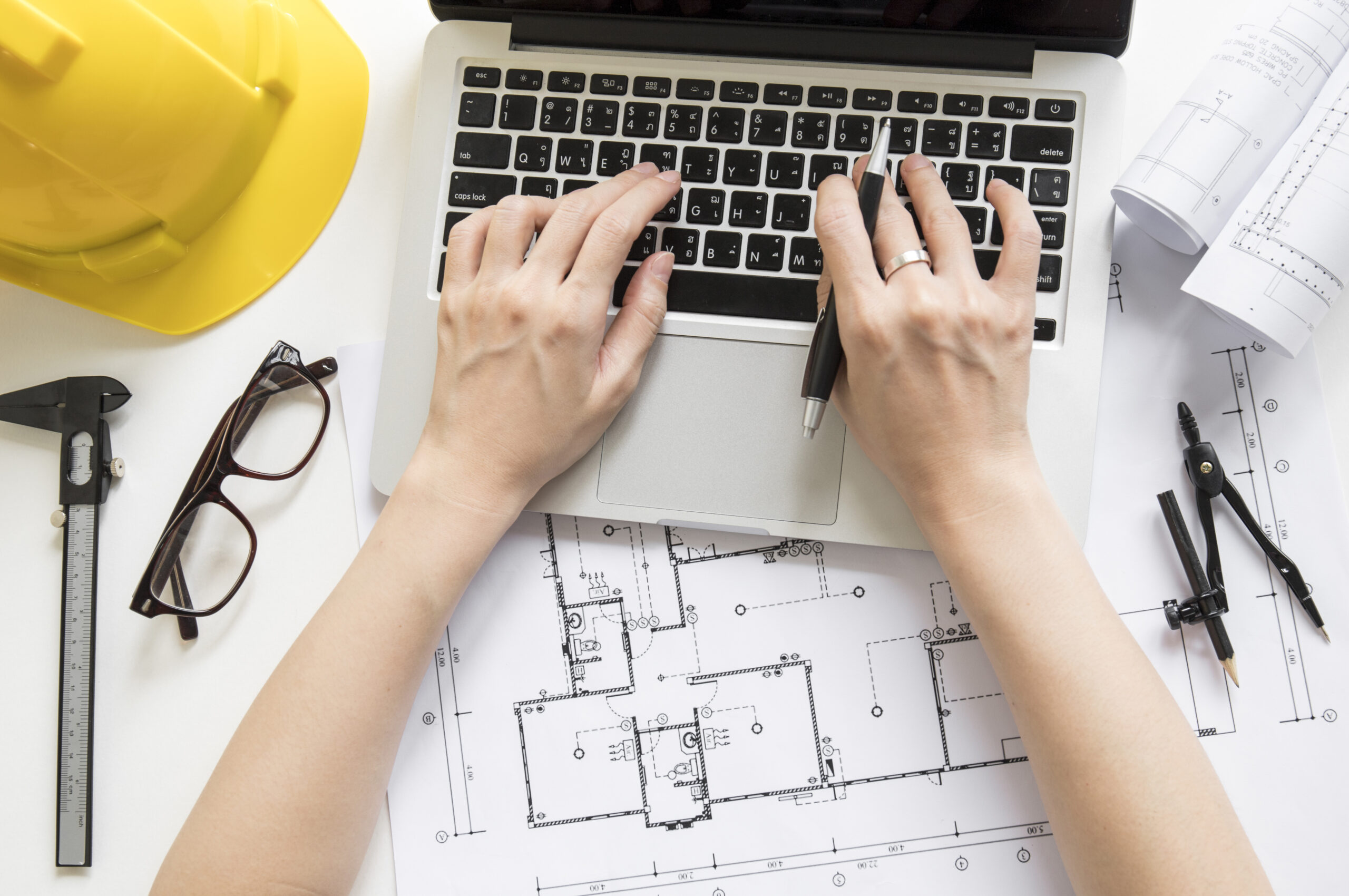 A person types on a laptop while reviewing architectural plans